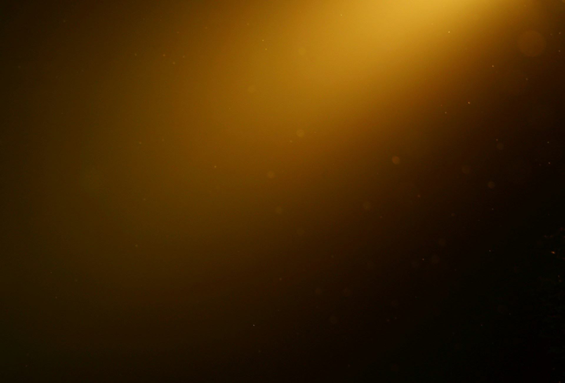 A field of warm amber light falling across darkness from the upper right, with fine dust suspended in the beam